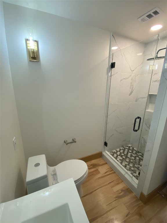 bathroom featuring hardwood / wood-style flooring, a shower with shower door, and toilet