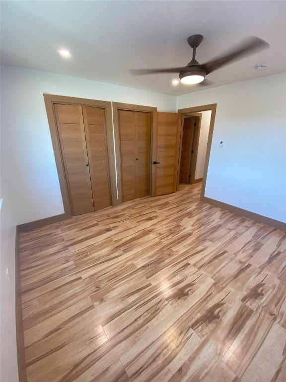 unfurnished bedroom featuring multiple closets, ceiling fan, and light hardwood / wood-style floors