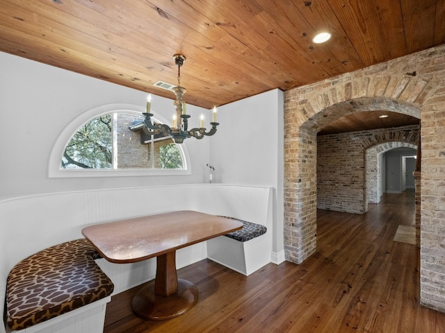 dining space with wood ceiling, dark wood-type flooring, brick wall, breakfast area, and a chandelier