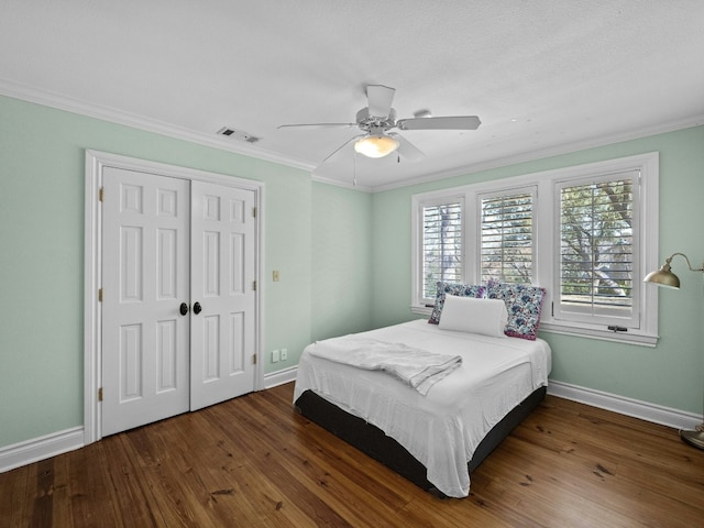 bedroom featuring dark wood-type flooring, ornamental molding, a closet, and ceiling fan