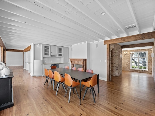 dining area with an inviting chandelier, beam ceiling, light wood-type flooring, and brick wall