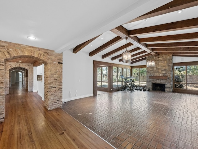 unfurnished living room with a notable chandelier, a stone fireplace, and lofted ceiling with beams