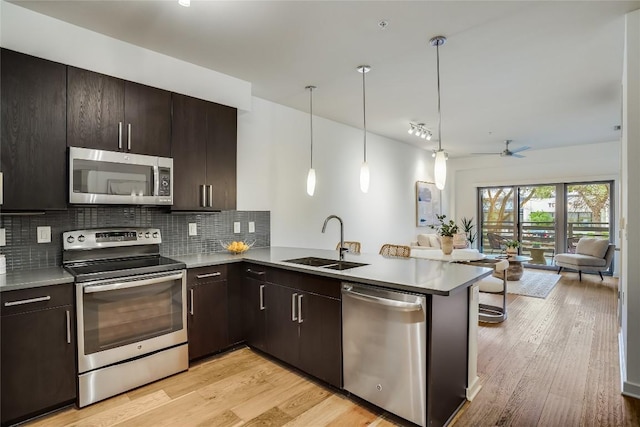 kitchen featuring sink, backsplash, kitchen peninsula, stainless steel appliances, and light wood-type flooring