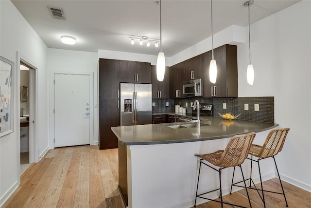 kitchen with appliances with stainless steel finishes, sink, hanging light fixtures, kitchen peninsula, and dark brown cabinets