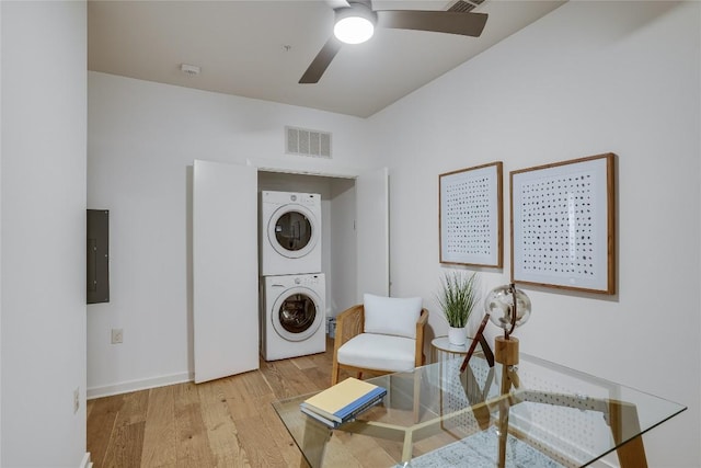 clothes washing area featuring electric panel, stacked washer and clothes dryer, ceiling fan, and light wood-type flooring