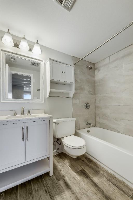 full bathroom with tiled shower / bath, hardwood / wood-style floors, vanity, and toilet