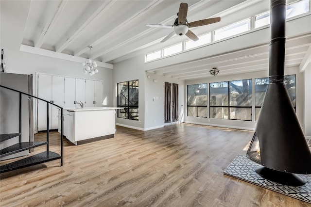 living room featuring ceiling fan with notable chandelier, light hardwood / wood-style flooring, beamed ceiling, and a wood stove