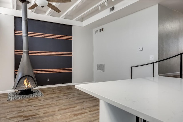 interior space featuring wood-type flooring, rail lighting, a wood stove, and ceiling fan