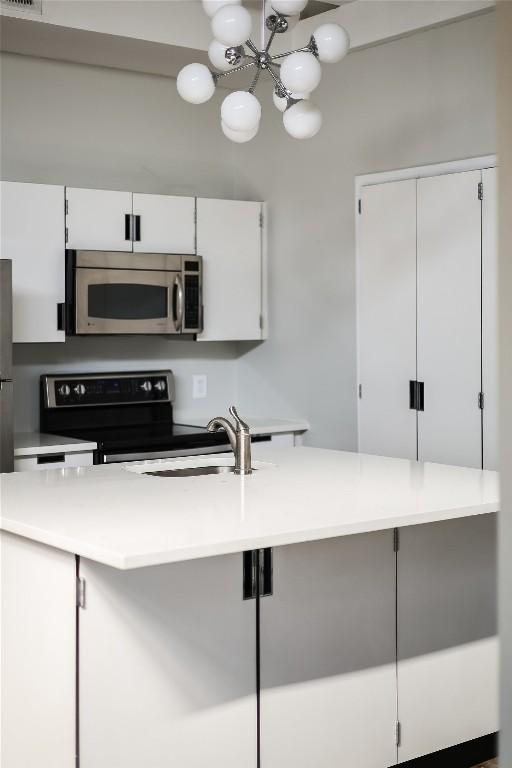 kitchen with sink, an inviting chandelier, white cabinets, and electric range