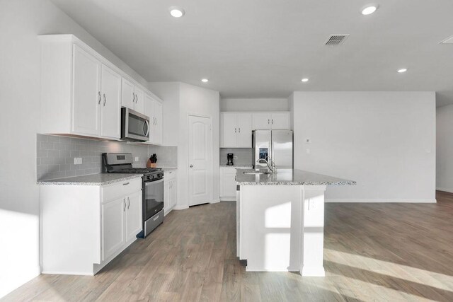 kitchen featuring white cabinets, light stone counters, light hardwood / wood-style floors, stainless steel appliances, and a center island with sink