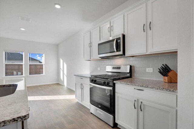 kitchen featuring white cabinetry, light stone counters, stainless steel appliances, light hardwood / wood-style floors, and decorative backsplash