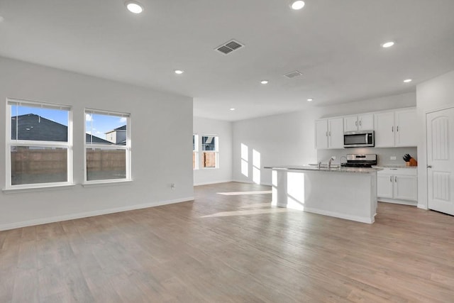 kitchen featuring light hardwood / wood-style flooring, appliances with stainless steel finishes, light stone counters, white cabinets, and a center island with sink