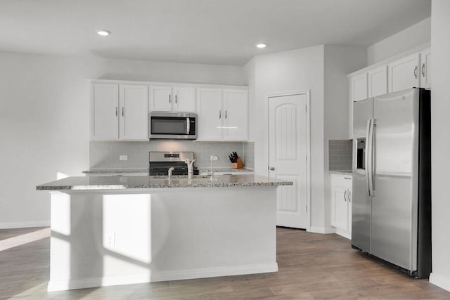 kitchen with light stone counters, a center island with sink, appliances with stainless steel finishes, white cabinets, and backsplash