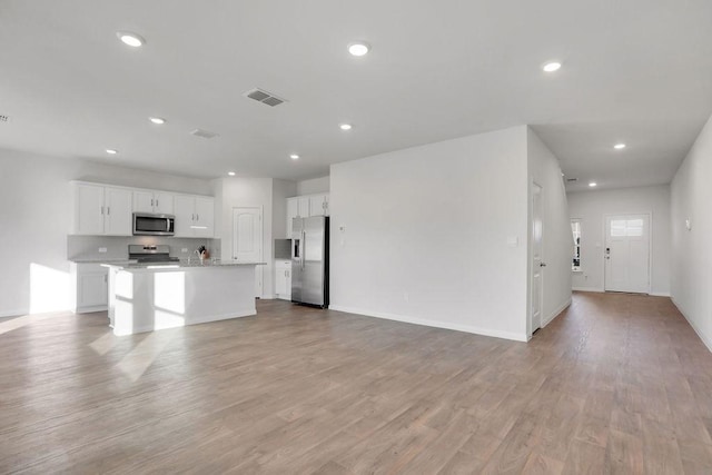 kitchen featuring stainless steel appliances, an island with sink, white cabinets, and light hardwood / wood-style flooring