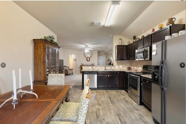 kitchen with appliances with stainless steel finishes, decorative backsplash, kitchen peninsula, light stone countertops, and light wood-type flooring