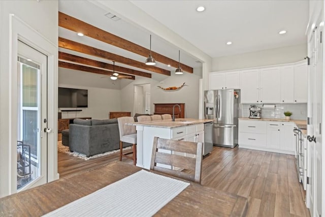 kitchen with a kitchen bar, white cabinetry, light stone counters, appliances with stainless steel finishes, and an island with sink