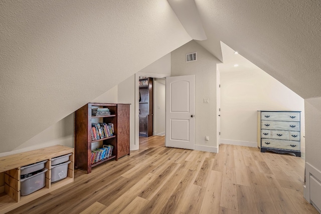 additional living space with vaulted ceiling, a textured ceiling, and light wood-type flooring