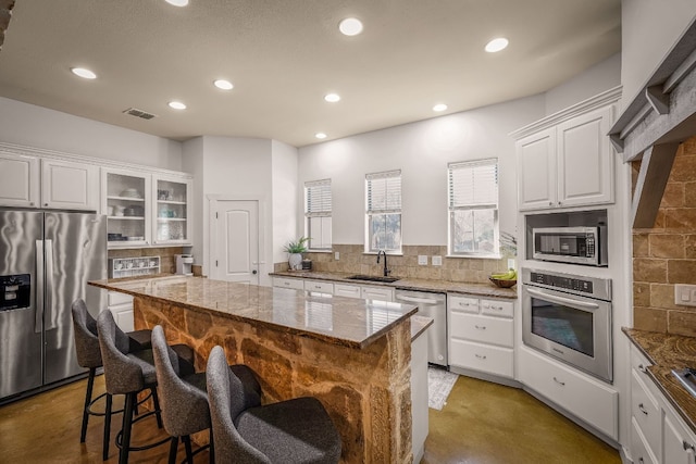 kitchen featuring sink, white cabinetry, light stone counters, a center island, and stainless steel appliances