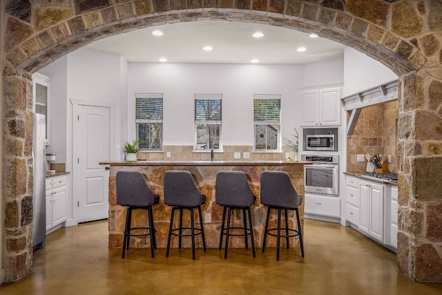 kitchen with stainless steel appliances, white cabinetry, a kitchen island, and concrete floors