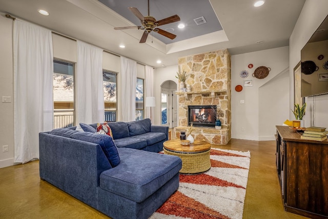 living room with a tray ceiling, a fireplace, concrete flooring, and ceiling fan