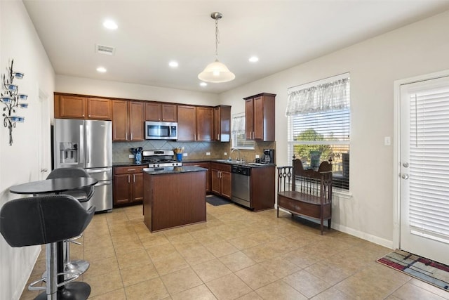 kitchen with pendant lighting, sink, appliances with stainless steel finishes, a kitchen island, and decorative backsplash