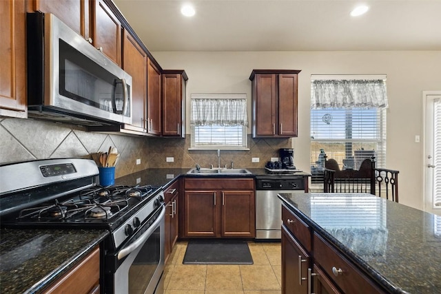 kitchen with sink, light tile patterned floors, stainless steel appliances, decorative backsplash, and dark stone counters