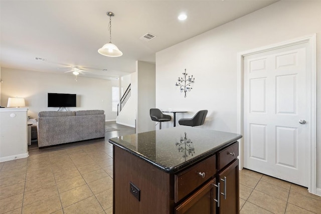 kitchen with light tile patterned flooring, decorative light fixtures, a center island, dark brown cabinets, and dark stone countertops