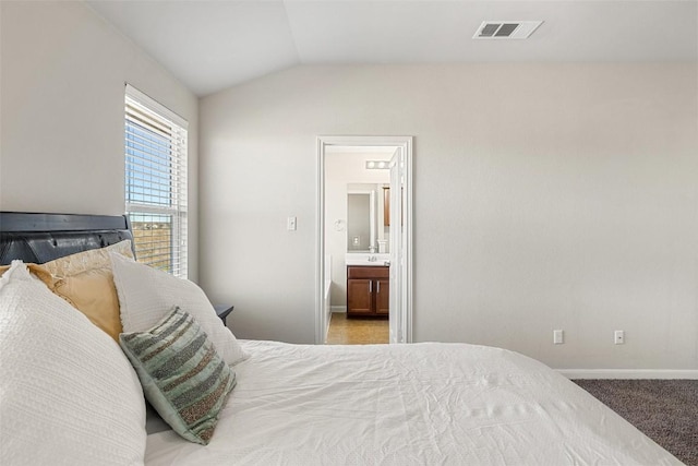 carpeted bedroom featuring ensuite bath and lofted ceiling