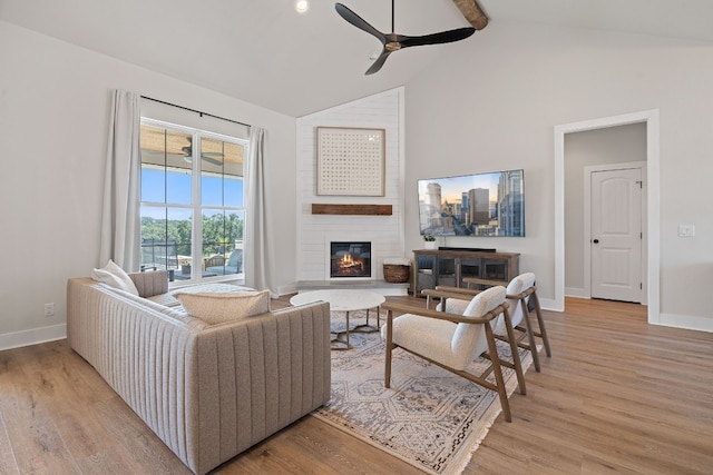 living room featuring beamed ceiling, a large fireplace, ceiling fan, and light hardwood / wood-style flooring