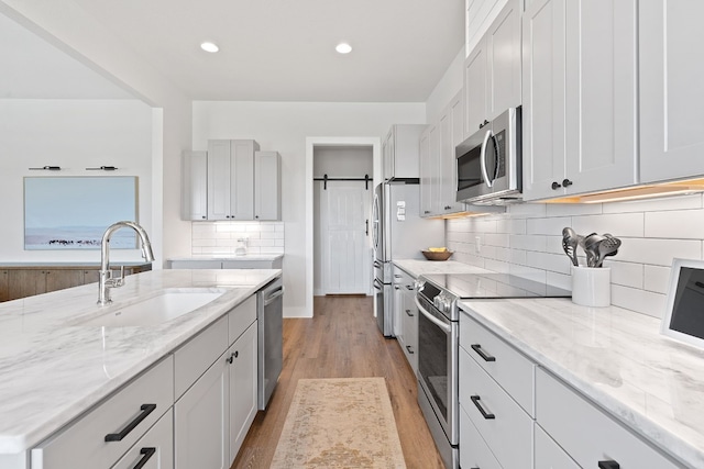 kitchen featuring light stone counters, sink, a barn door, and appliances with stainless steel finishes