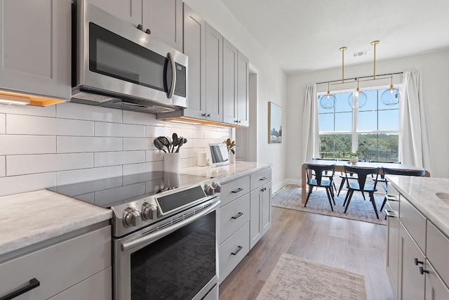 kitchen with pendant lighting, light hardwood / wood-style flooring, appliances with stainless steel finishes, backsplash, and light stone countertops