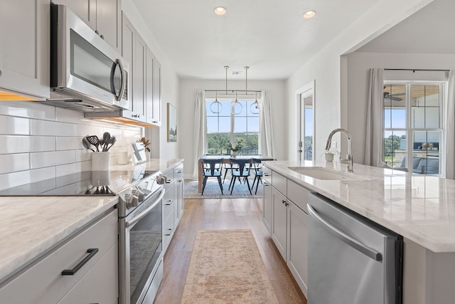 kitchen featuring pendant lighting, sink, stainless steel appliances, light stone countertops, and light wood-type flooring