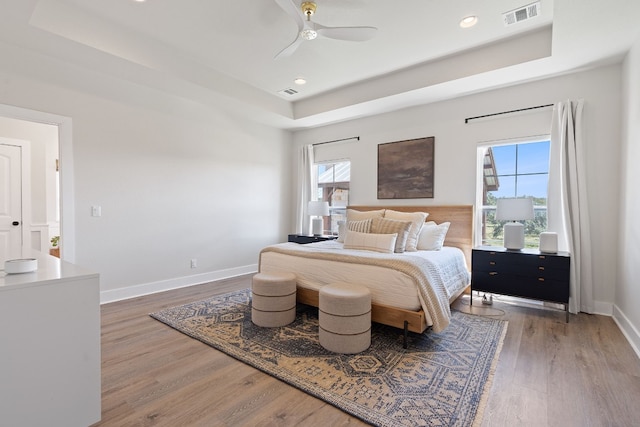 bedroom with dark hardwood / wood-style flooring, a tray ceiling, and ceiling fan