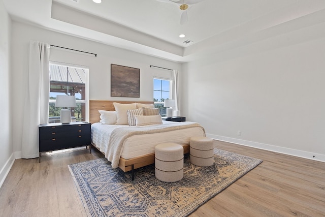 bedroom with ceiling fan, a tray ceiling, dark hardwood / wood-style flooring, and multiple windows