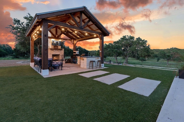 yard at dusk featuring a gazebo, a patio, an outdoor stone fireplace, and a bar