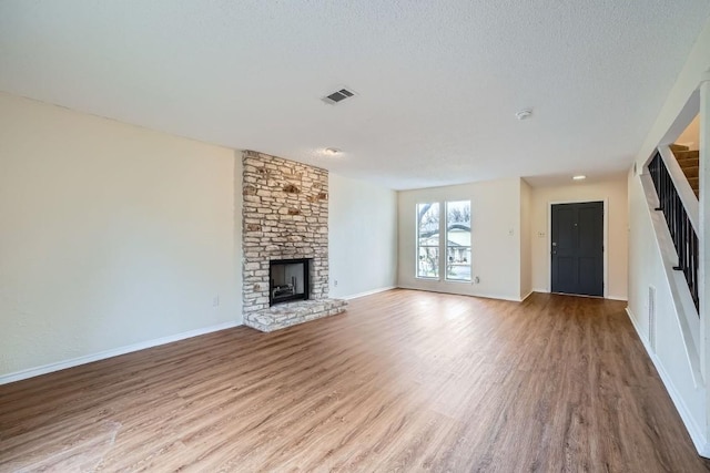 unfurnished living room featuring a stone fireplace, a textured ceiling, and light wood-type flooring