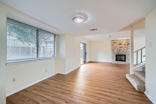 unfurnished living room featuring hardwood / wood-style flooring, plenty of natural light, and a stone fireplace