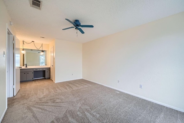 unfurnished bedroom with sink, ceiling fan, ensuite bathroom, a textured ceiling, and light carpet