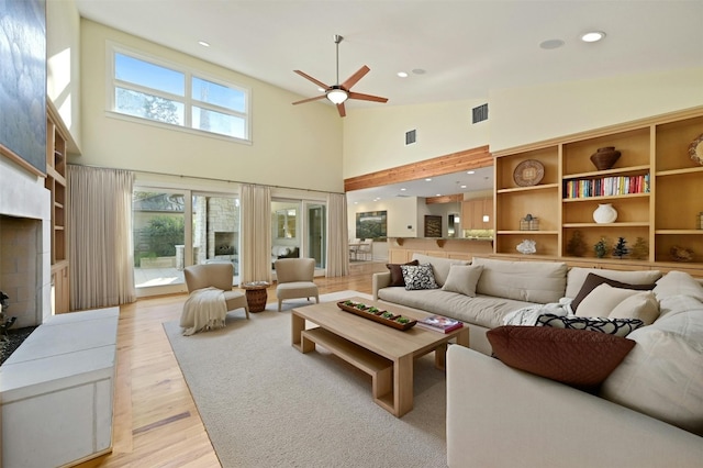 living room with a towering ceiling, ceiling fan, and light hardwood / wood-style flooring