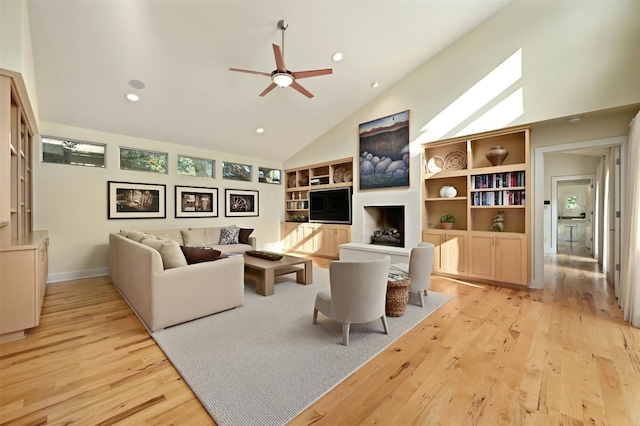 living room with ceiling fan, a tiled fireplace, high vaulted ceiling, and light hardwood / wood-style flooring