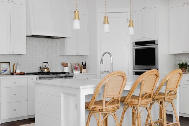 kitchen featuring white cabinetry, backsplash, a kitchen bar, a kitchen island with sink, and custom range hood