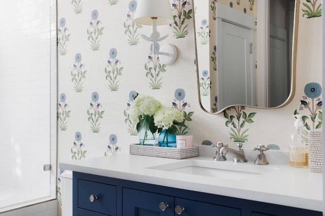 bathroom featuring walk in shower, vanity, and wallpapered walls