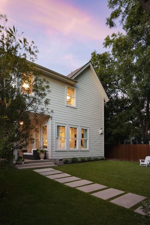 back house at dusk featuring a lawn