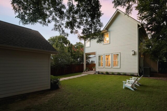 back house at dusk featuring central AC and a lawn