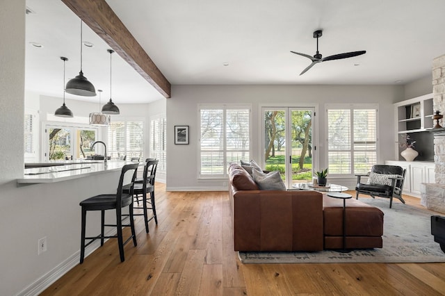 living room with ceiling fan, beam ceiling, sink, and light hardwood / wood-style flooring