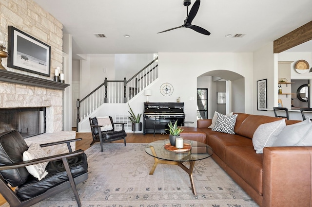 living room with ceiling fan, a stone fireplace, and light wood-type flooring