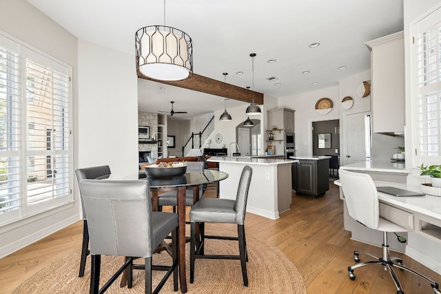 dining room featuring ceiling fan, a stone fireplace, and light hardwood / wood-style floors