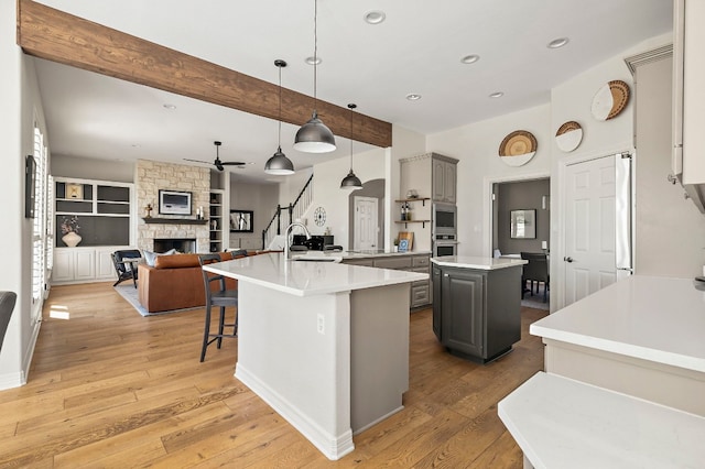 kitchen featuring light wood-type flooring, gray cabinets, an island with sink, pendant lighting, and a fireplace