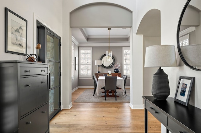 interior space with ornamental molding, a raised ceiling, and light hardwood / wood-style flooring