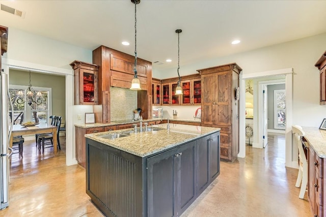 kitchen featuring sink, light stone counters, hanging light fixtures, a center island with sink, and a notable chandelier